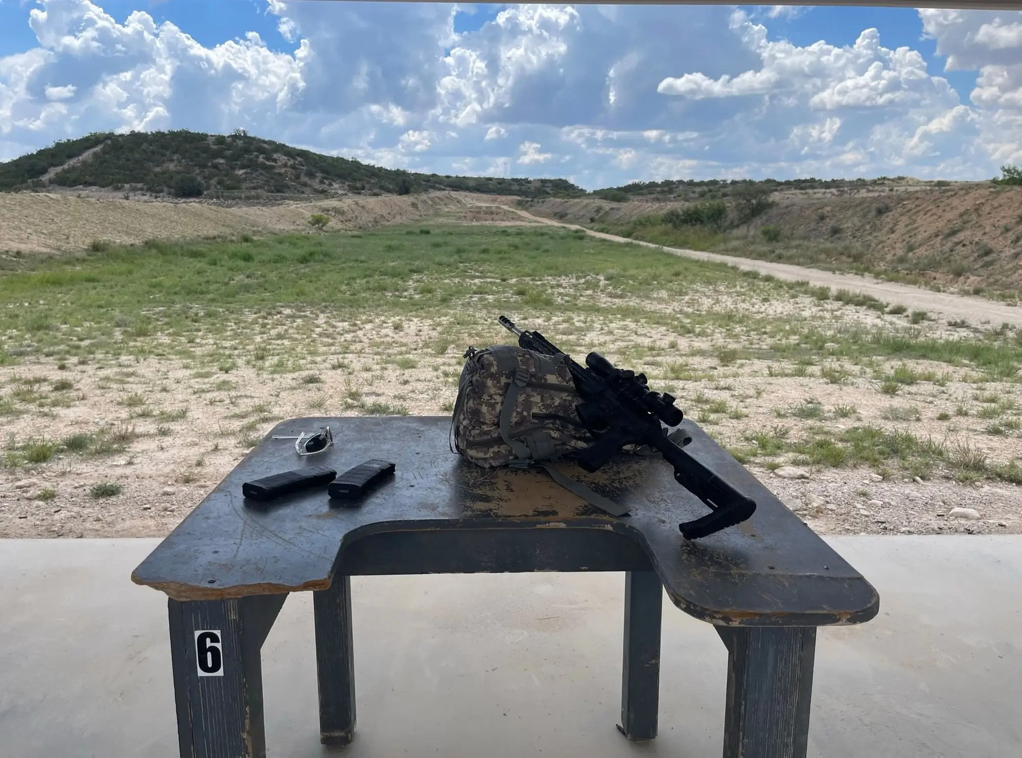 Un fucile e una pistola appoggiati sul tavolo della linea di tiro, davanti alla collina di terra